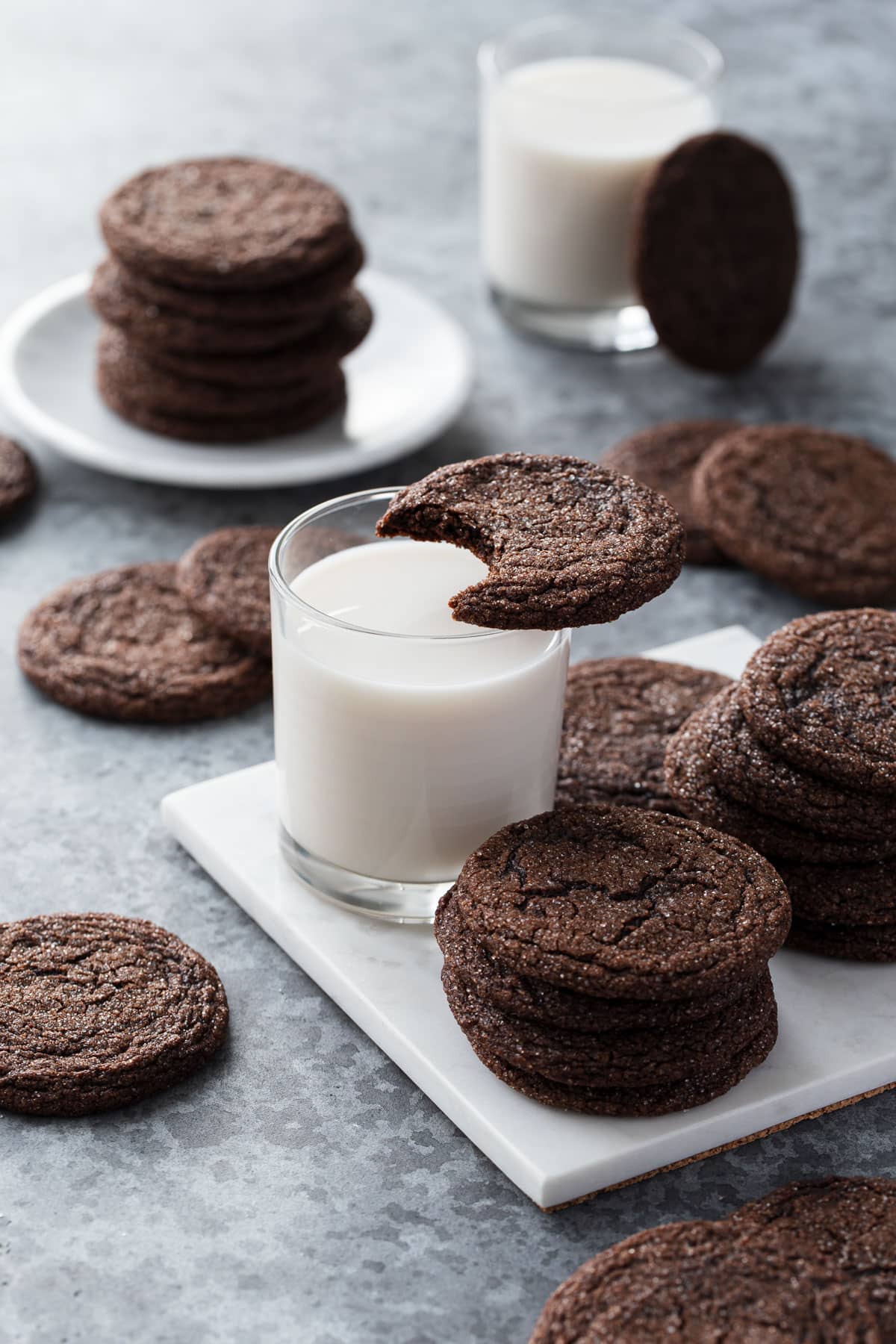 Chewy Chocolate Molasses Cookie with a bite taken out of it resting on top of a glass of milk, more cookies arranged around it.