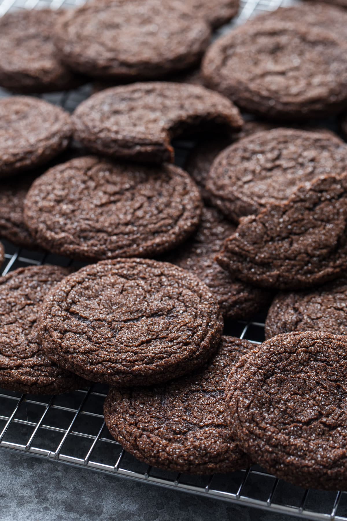 Chewy Chocolate Molasses Cookies piled on a wire baking rack, one cookie on top with a bite out of it.