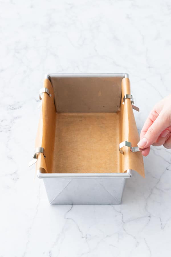 Securing the parchment paper to the sides of the loaf pan with clips.