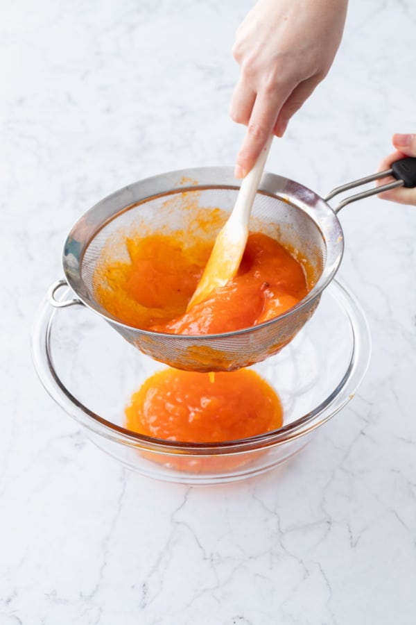 Straining persimmon pulp through a fine mesh sieve to make a smooth puree.