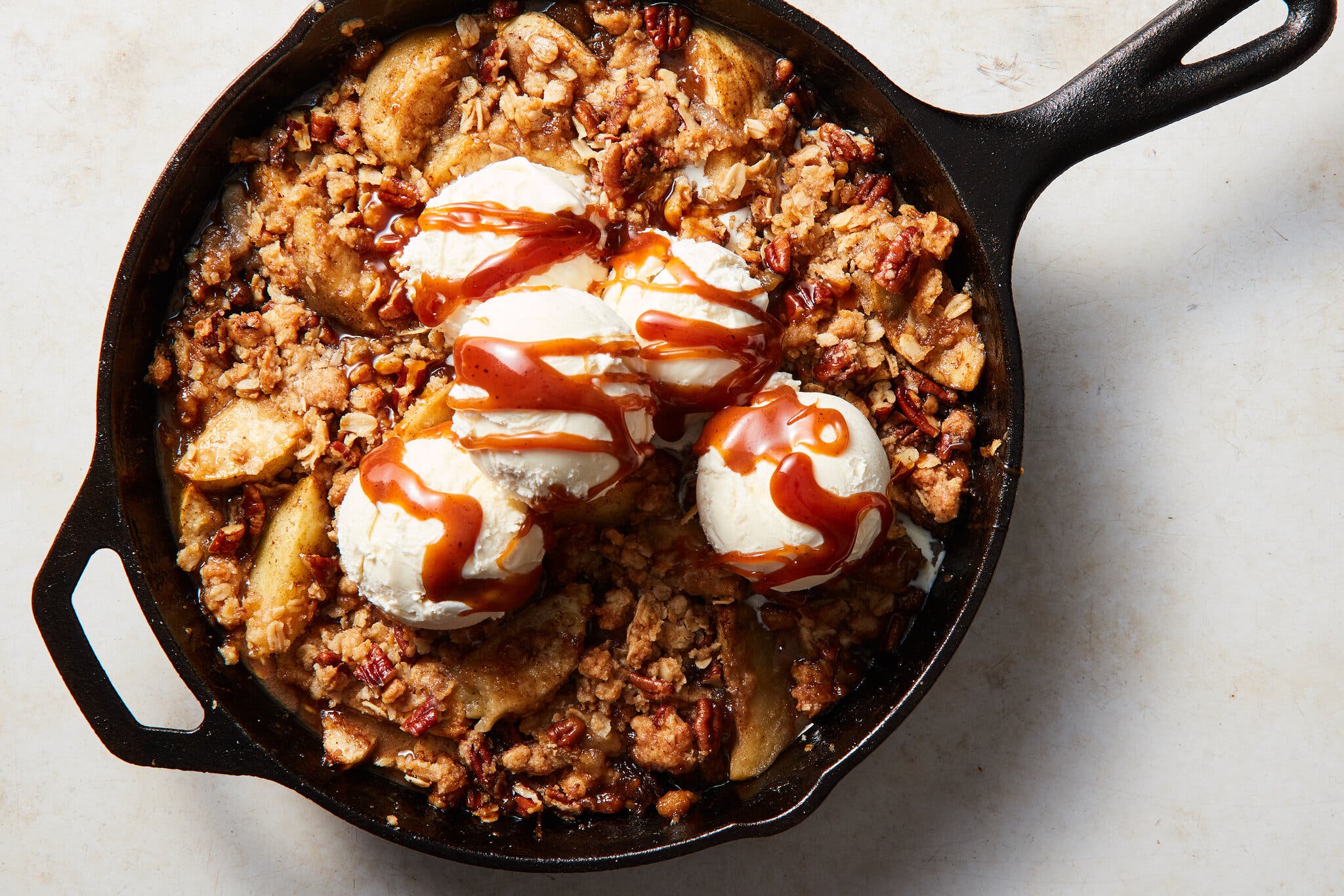 A cast-iron skillet filled with baked apples topped with a crisp crumble and scoops of vanilla ice cream.