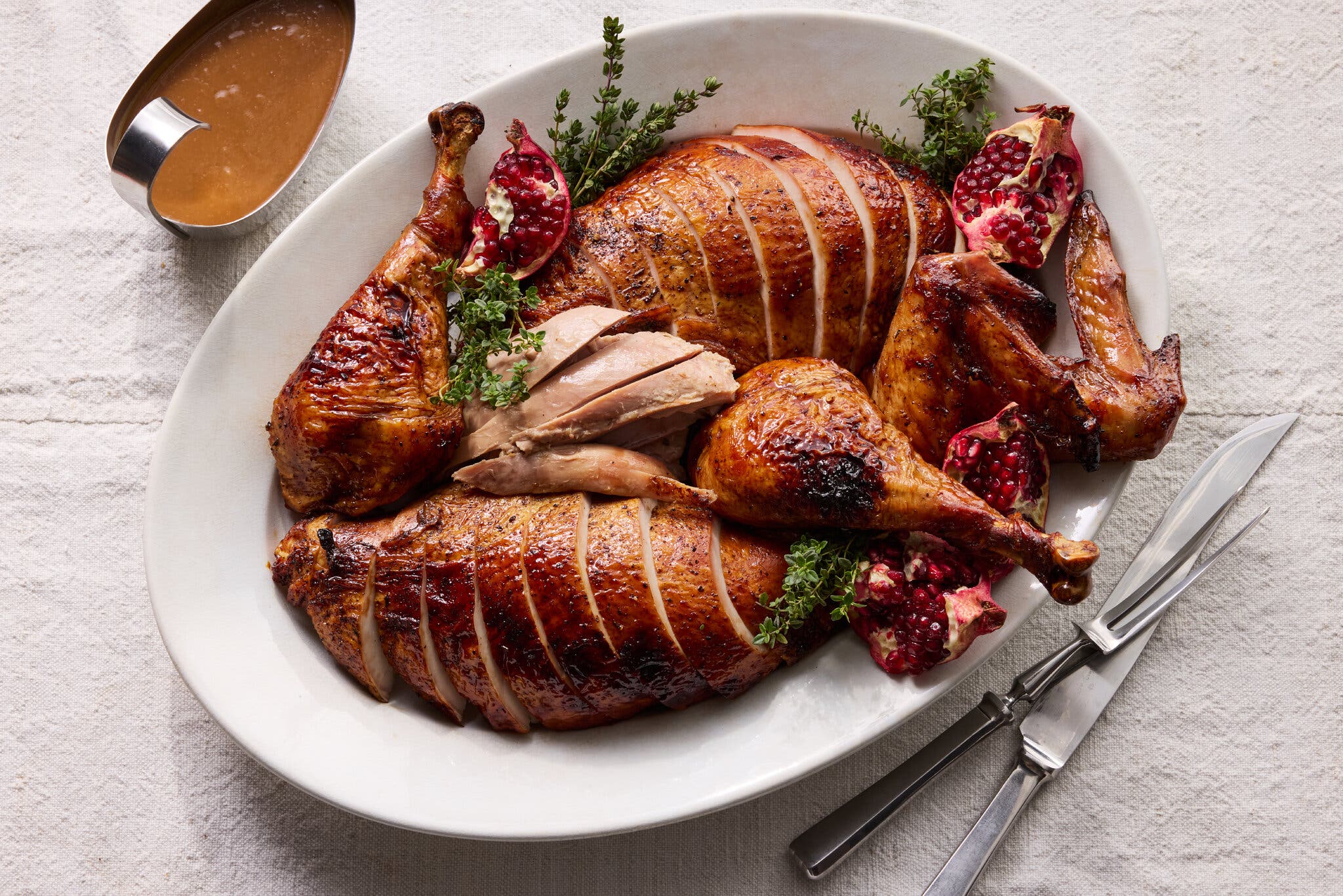 A platter of sliced roasted turkey breast and dark meat, garnished with sprigs of thyme and crimson pomegranate pieces.