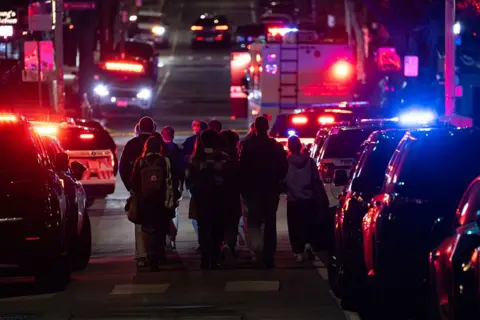 Anadolu via Getty Images Ambulances and police cars line a street at night with red and blue lights in the background as emergency personnel escort students from one of the buildings of Brown University in Providence, Rhode Island, on 13 December