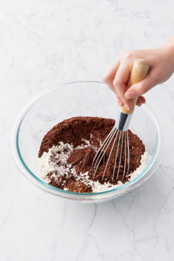 Whisking dry ingredients with a whisk in a glass mixing bowl.