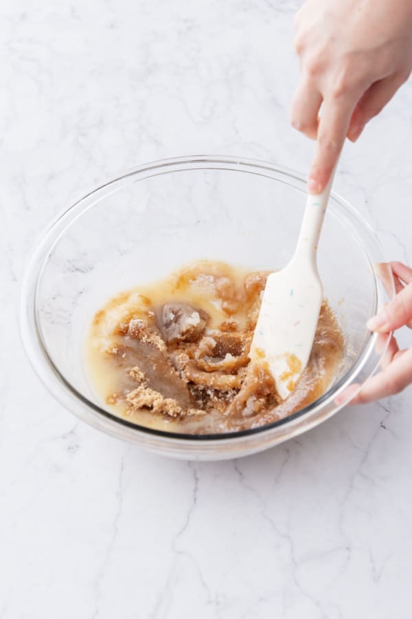 Mixing melted butter with brown and white sugar in a glass mixing bowl.