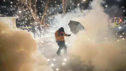 Reuters A protester on a snowy street uses an umbrella to shield themself from a cloud of tear gas and sparks in Minneapolis