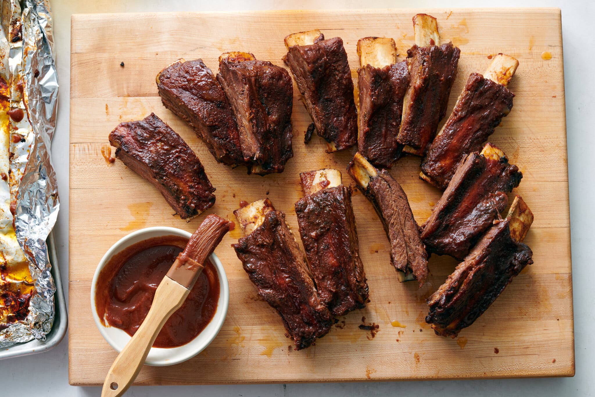 An overhead image of pork ribs on a cutting board next to a bowl of sauce.