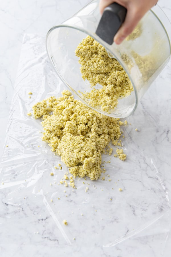 Pouring crumbly dough mixture onto a piece of plastic wrap.